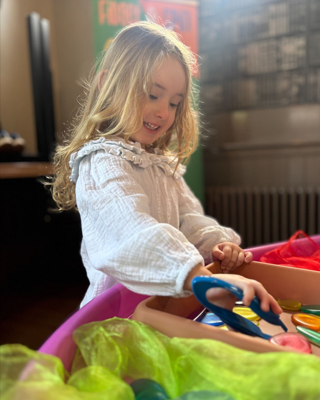 A child attending a Fidget and Spin Stay and Play session smiles while exploring colourful shapes and sensory scarves.