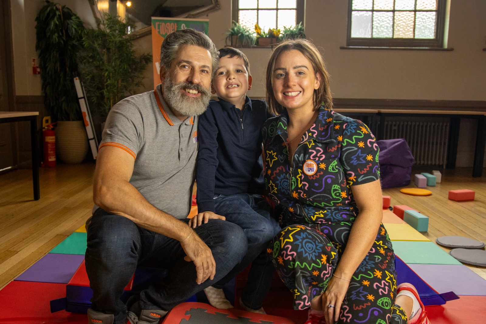 Fidget and Spin founders Anthony and Caitlin smile with their son Remy in the sensory Stay and Play space.