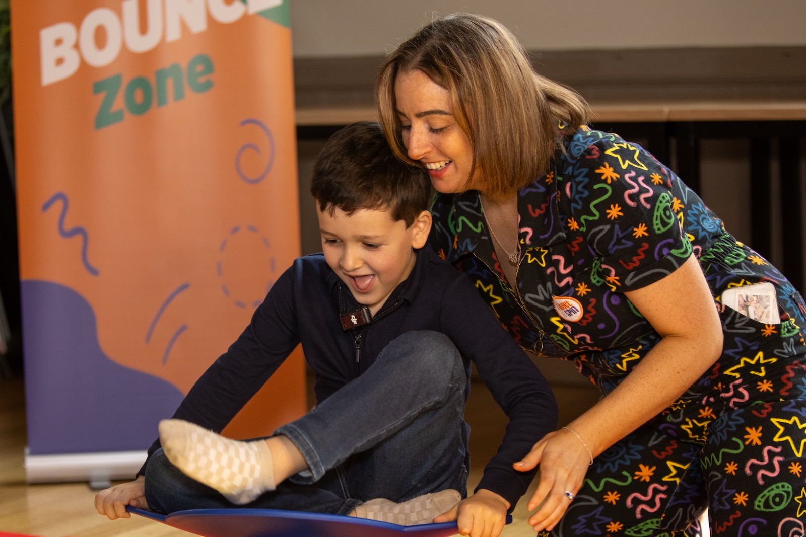 A child attending a Fidget and Spin Stay and Play session enjoys a spinning chair with support from Caitlin.